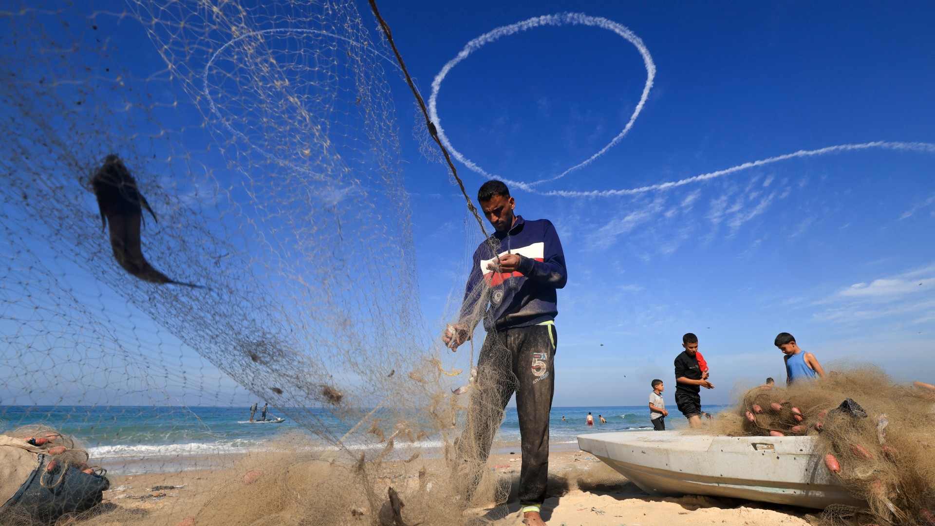 صيادون فلسطينيون يفرزون صيدهم في دير البلح بينما تحلق نفاثات طائرة إسرائيلية في السماء في 30 تشرين الثاني/نوفمبر (AFP/Mahmud Hams)